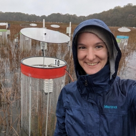Genevieve Noyce stands next to a red cylindrical chamber used to measure greenhouse gas emissions